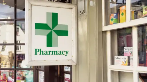 Getty Images A wooden sign, depicting the traditional green pharmacy cross, on a small, community pharmacy in England 