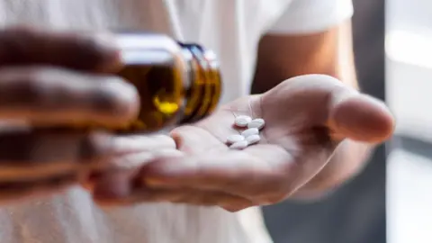 Getty Images Person tipping white pills out of a brown bottle and into the palm of their hand