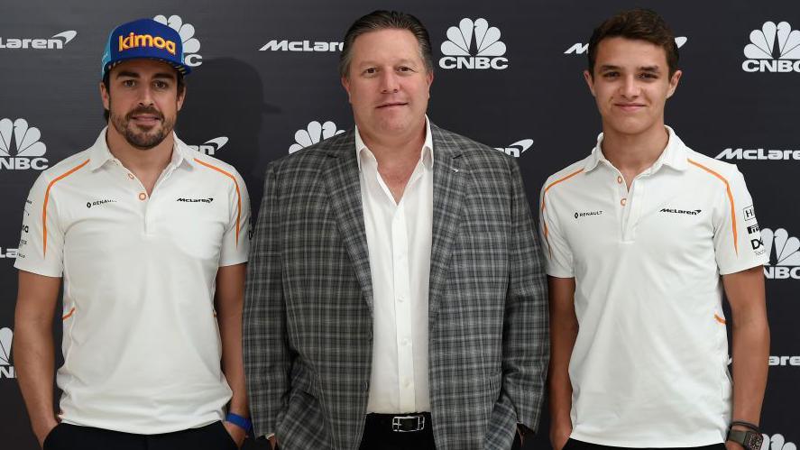 Fernando Alonso, Zak Brown and Lando Norris stood next to each other at Abu Dhabi in 2018. Alonso and Norris are both wearing McLaren polo shirts