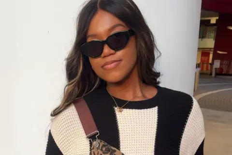 Branneisha Cooper A woman with dark hair in sunglasses, a black and white striped jumper and leopard-print dungarees